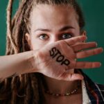 Close-up of a woman holding her hand marked with 'stop' in front of her face, symbolizing protest and strength.